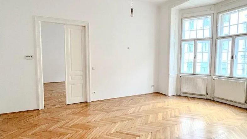 Helles Wohnzimmer mit Fischgrätparkettboden und einem Erkerfenster, das viel Tageslicht hereinlässt.