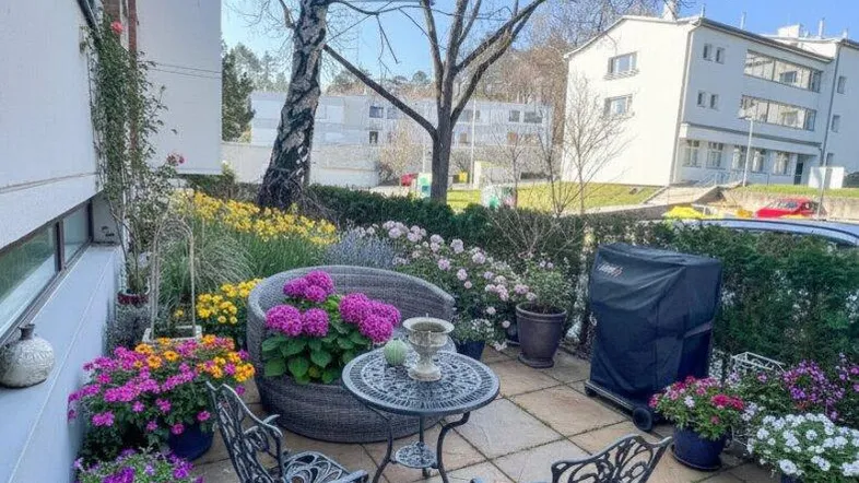 Gemütliche gepflasterte Terrasse mit Gartenmöbeln und vielen bunten Blumen in Töpfen.