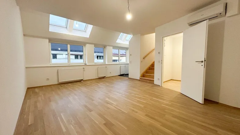 Helles Wohnzimmer mit Holzparkettboden, Dachfenstern und Zugang zu einer Holztreppe.