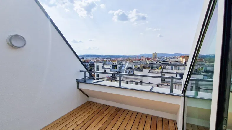 Heller Balkon mit Holzboden und weitem Blick über die Stadt und die umliegenden Dächer.