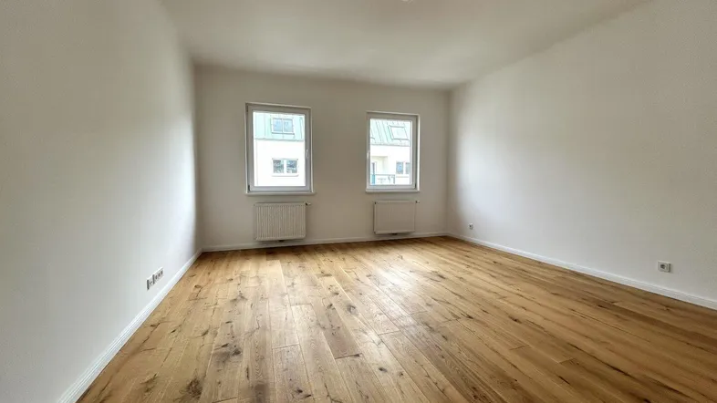 Helles, leeres Zimmer mit neuem Holzboden und zwei Fenstern, bereit zur individuellen Gestaltung.
