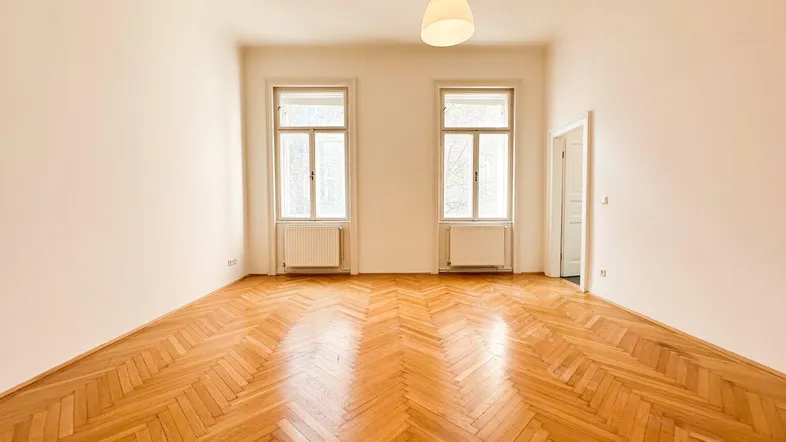 Helles Zimmer mit Fischgrätparkettboden und zwei großen Fenstern, bereit zur individuellen Gestaltung.