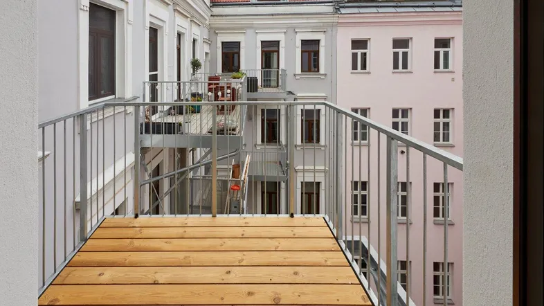 Neuer Holzbalkon mit Metallgeländer und Blick auf die umliegenden Gebäude des Innenhofs.