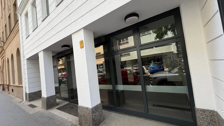 Eingangsbereich eines modernen Gebäudes mit großen Glasfronten und weißer Fassade.