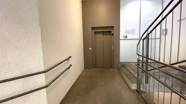 Eingangsbereich eines Gebäudes mit Aufzug, Treppe und barrierefreier Rampe für den Zugang zu den Etagen.