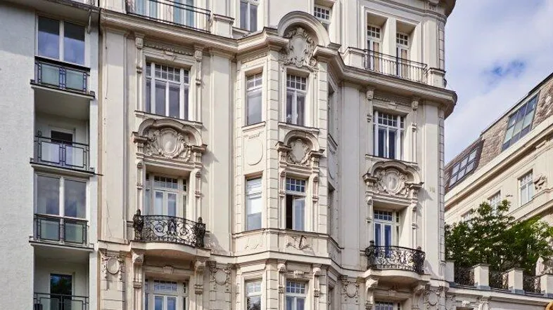 Elegantes Altbaugebäude mit reich verzierten Fassaden, Balkonen und Dachterrassenbegrünung in urbaner Umgebung.