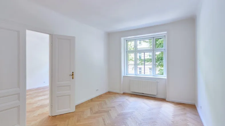 Helles Zimmer mit Fischgrätparkett und weiß gestrichenen Wänden, bereit zur individuellen Gestaltung.