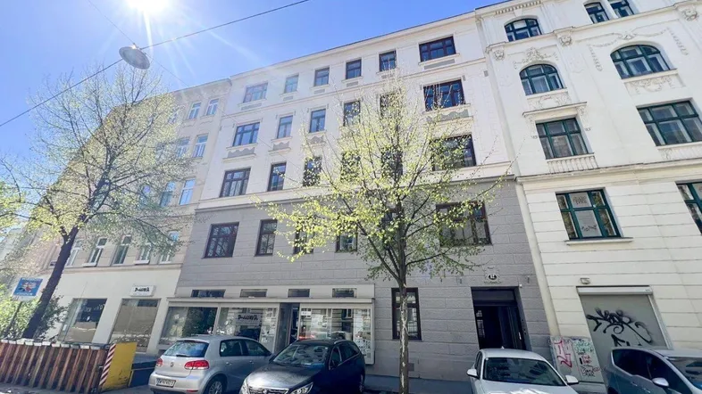 Sonnenbeschienene Fassade eines Mehrfamilienhauses mit geparkten Autos auf der Straße.