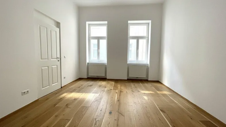 Helles Zimmer mit neuem Holzboden und zwei Fenstern, ideal als Wohn- oder Schlafzimmer.