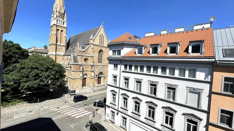 Blick von oben auf eine Straße mit einem historischen Gebäude und einer Kirche im Hintergrund unter blauem Himmel.