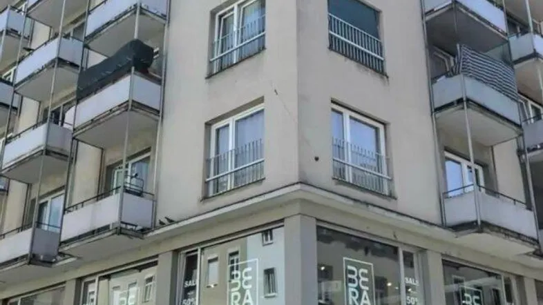 Mehrstöckiges Wohngebäude mit zahlreichen Balkonen und Geschäften im Erdgeschoss in urbaner Umgebung.