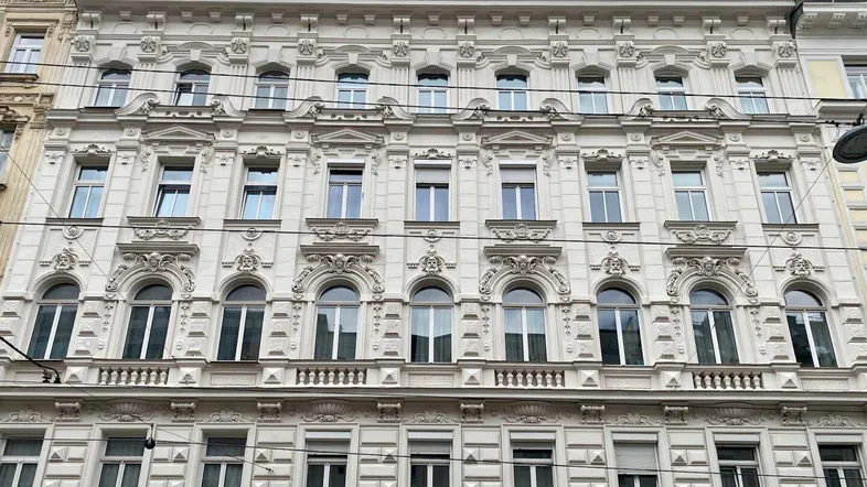 Detailansicht einer reich verzierten Fassade eines Altbaus mit vielen Fenstern und Stuckelementen.