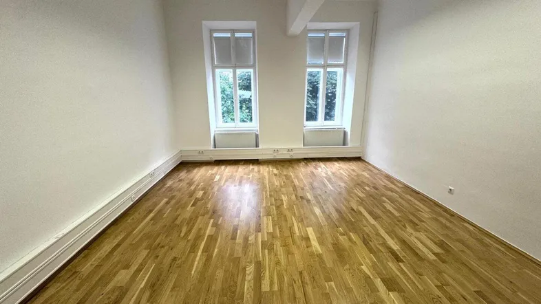 Heller Büroraum mit zwei großen Fenstern, Holzboden und modernen Deckenleuchten, ideal für produktives Arbeiten.