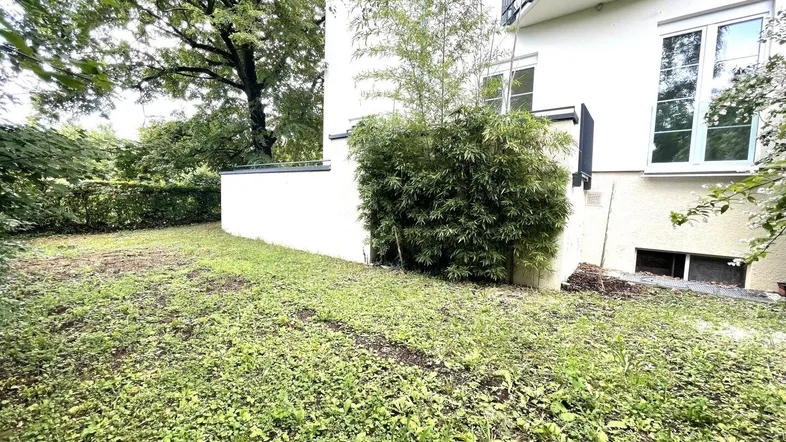 Gartenbereich neben dem Gebäude mit Rasenfläche und üppiger Bepflanzung, ideal für Entspannung im Freien.