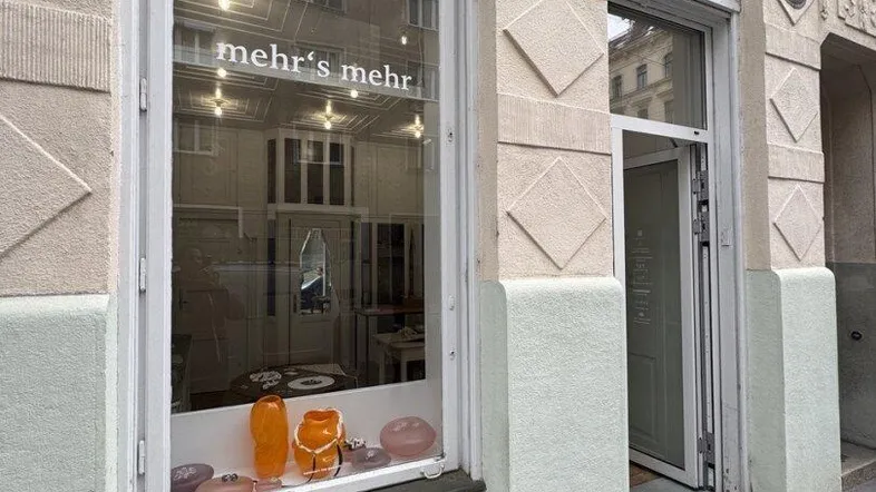 Fassade eines Gebäudes mit einem Schaufenster und einem Eingang, davor eine kleine Holzbank.