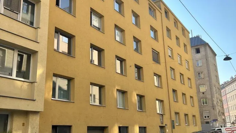 Gelbe Fassade eines Mehrfamilienhauses mit vielen Fenstern und parkenden Autos auf der Straße.