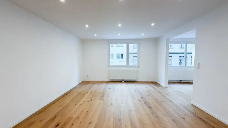 Heller, leerer Raum mit modernem Holzparkettboden und Einbaustrahlern an der Decke.