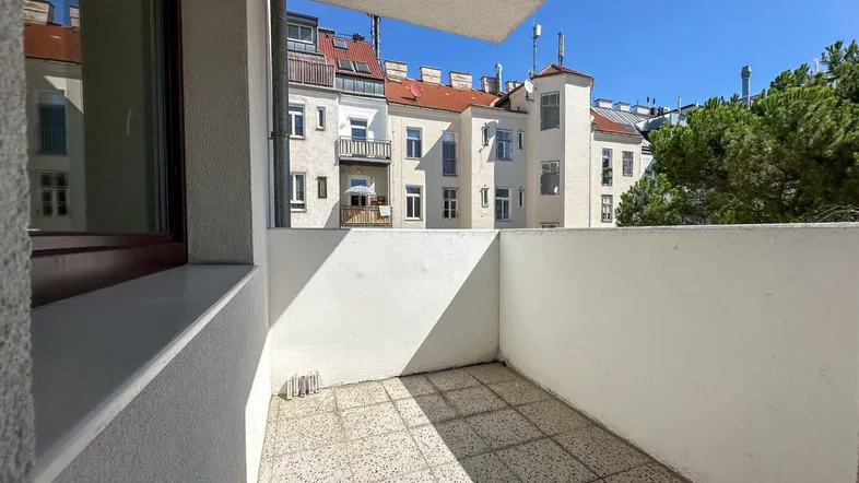 Heller Balkon mit Fliesenboden und Blick auf die umliegenden Gebäude unter blauem Himmel.