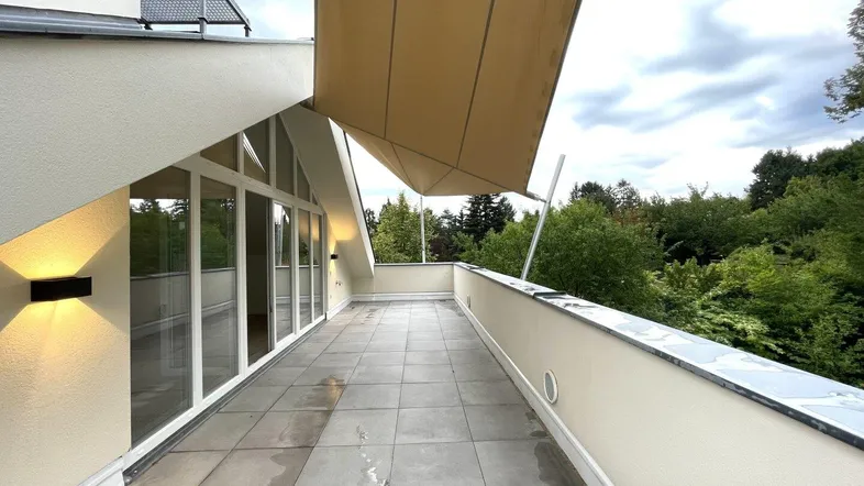 Große geflieste Terrasse mit ausfahrbarer Markise und weitem Blick ins Grüne.