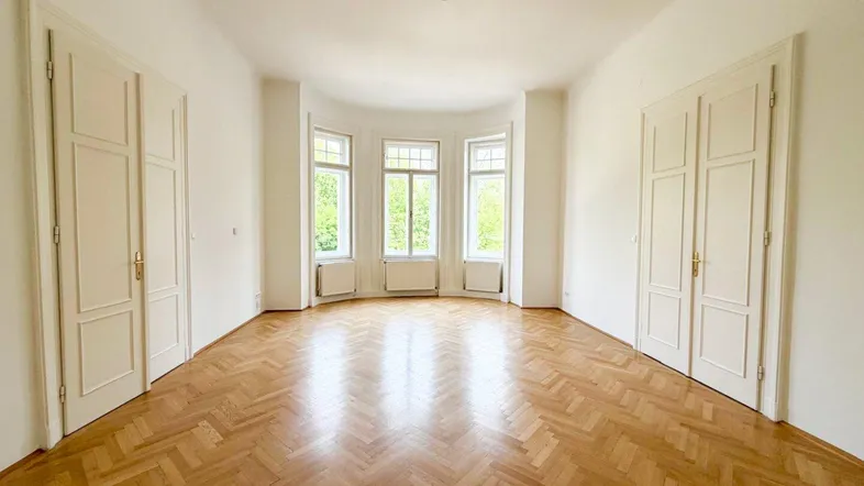 Helles, leeres Wohnzimmer mit Fischgrätparkett, hohen Decken und einem schönen Erkerfenster.