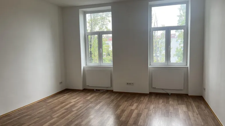 Helles Zimmer mit zwei großen Fenstern, Laminatboden und weißen Wänden, bereit zum Einzug.