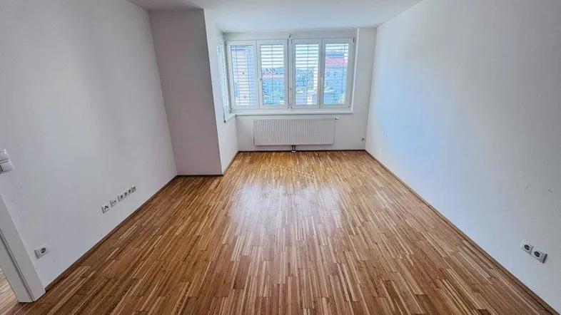 Helles Schlafzimmer mit Parkettboden, weißen Wänden und einem Fenster mit Blick nach draußen.