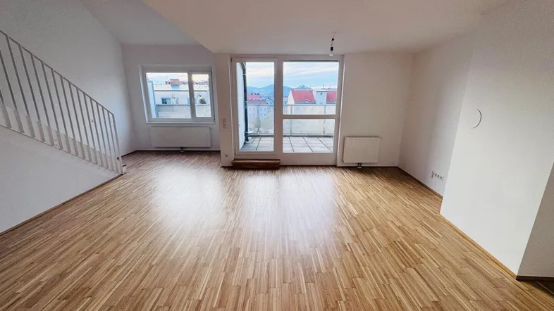 Helles Wohnzimmer mit Parkettboden, Zugang zur Terrasse und Treppe zum Obergeschoss.