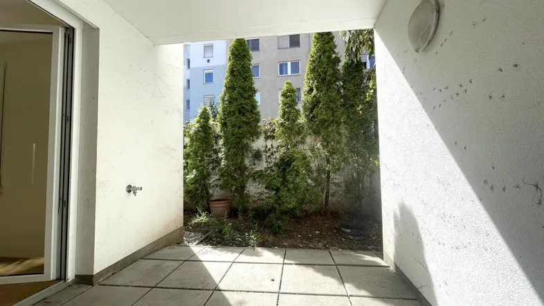Geräumige Terrasse mit Steinplatten und Blick auf eine grüne Hecke sowie das umliegende Gebäude.