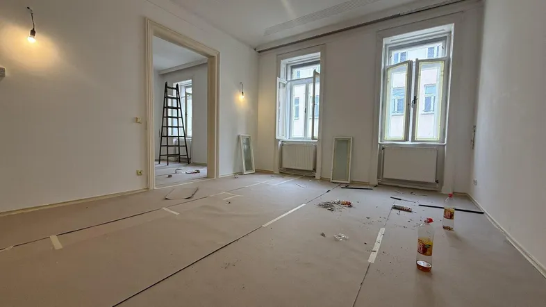 Geräumiger Raum in Renovierung mit hohen Decken und zwei großen Fenstern, bereit für die Gestaltung.