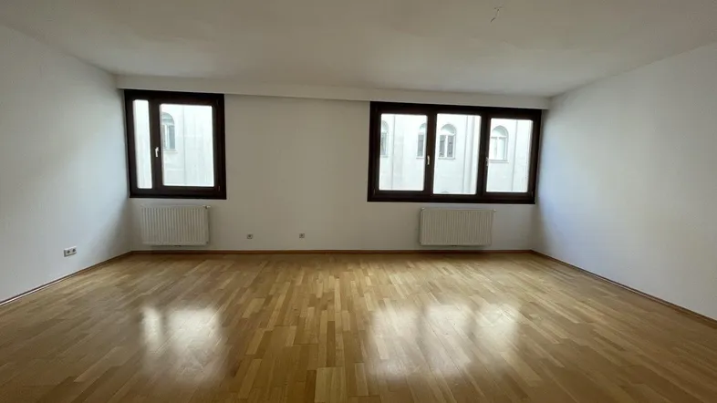 Helles Zimmer mit Parkettboden und zwei Fenstern, bereit zur individuellen Gestaltung.