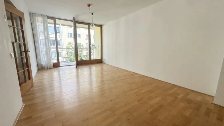 Helles, leeres Wohnzimmer mit Parkettboden und Zugang zu einem Balkon, bereit zur individuellen Gestaltung.