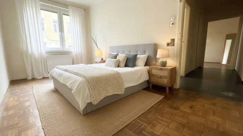 Helles Schlafzimmer mit Parkettboden, modernem Bett und Nachttischen, bietet eine ruhige Atmosphäre.
