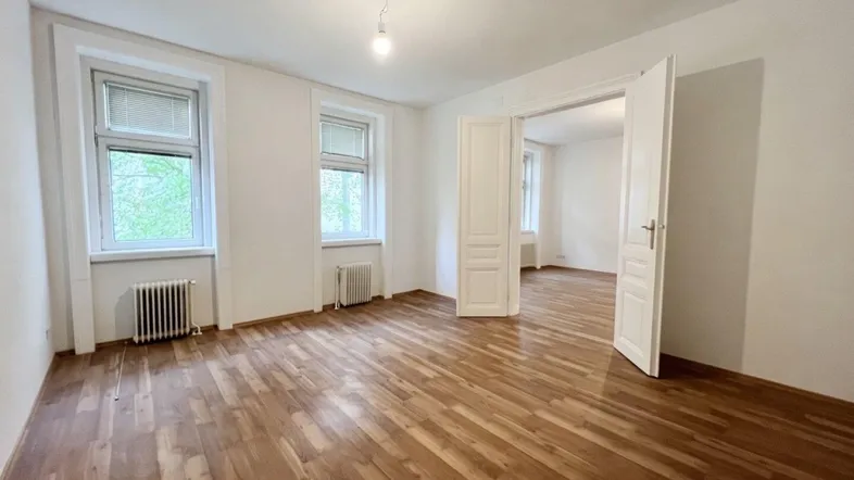 Helles Zimmer mit Parkettboden und zwei Fenstern, das vielseitig genutzt werden kann.