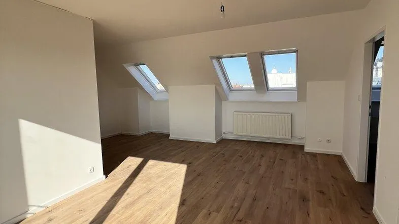 Helles Dachgeschosszimmer mit Holzboden und mehreren Dachfenstern, ideal als Wohn- oder Schlafbereich.