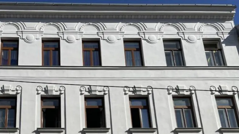 Historische Fassade eines Altbaus mit verzierten Fensterrahmen und weißem Putz.