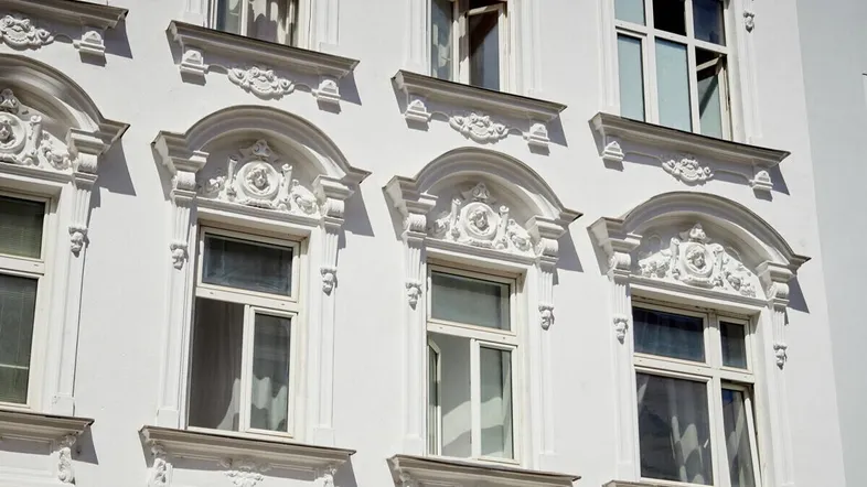 Weiße Fassade mit kunstvollen Stuckverzierungen und klassischen Fenstern, die den Altbaucharakter unterstreichen.