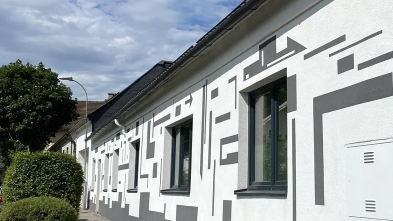 Moderne Fassade eines Gebäudes mit auffälligen geometrischen Mustern und dunklen Fenstern unter blauem Himmel.