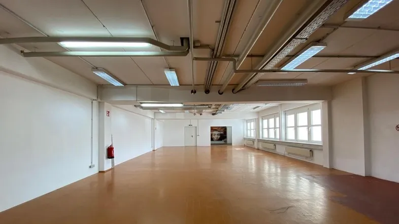 Großer, leerer Büroraum mit vielen Fenstern und sichtbaren Deckeninstallationen, bereit zur individuellen Gestaltung.