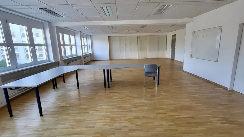Geräumiges Büro mit großen Fenstern, Holzboden und flexiblen Arbeitstischen, ideal für Teamarbeit.
