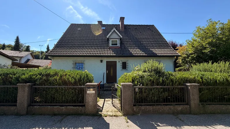 Vorderansicht eines Einfamilienhauses mit Satteldach, umgeben von einem gepflegten Vorgarten und Hecken.