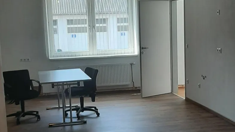 Geräumiger Büroraum mit dunklem Laminatboden, Fensterfront, Klimaanlage und einem blauen Teppich.