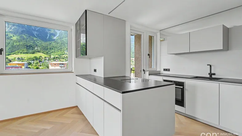 Moderne Küche mit weißer Kücheninsel, dunkler Arbeitsplatte und Bergblick durch das Fenster.