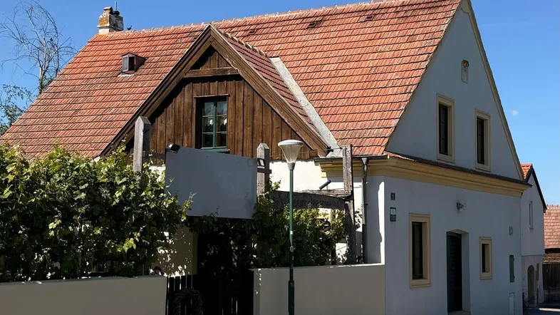 Traditionelles Haus mit Ziegeldach und Holzelementen, umgeben von einer niedrigen Mauer an der Straße.
