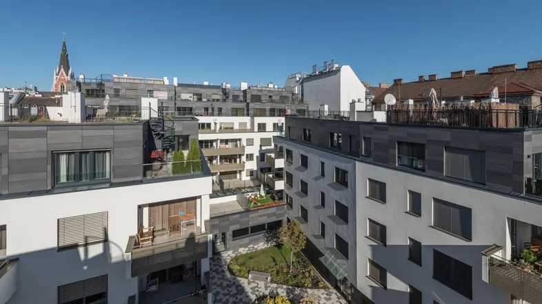 Blick auf die moderne Wohnanlage mit Innenhof und Kirchturm im Hintergrund.