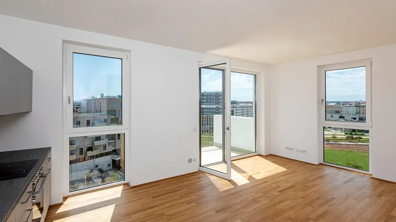 Heller offener Wohnbereich mit integrierter Küche, Parkettboden und Zugang zum Balkon.