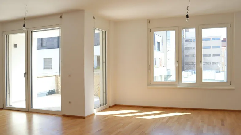 Helles Wohnzimmer mit Parkettboden, großen Fenstern und Zugang zu einem sonnigen Außenbereich.