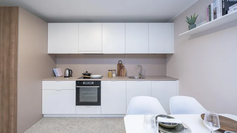 Moderne Küchenzeile mit weißen Schränken, integriertem Backofen und hellem Fliesenboden.