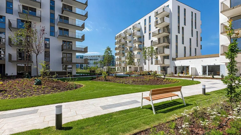 Moderne Wohnanlage mit gepflegter Grünfläche, Sitzbank und neuen Gebäuden unter blauem Himmel.