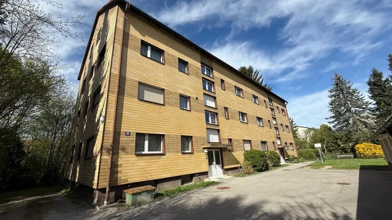 Mehrfamilienhaus mit gelber Holzfassade und grüner Umgebung unter blauem Himmel.