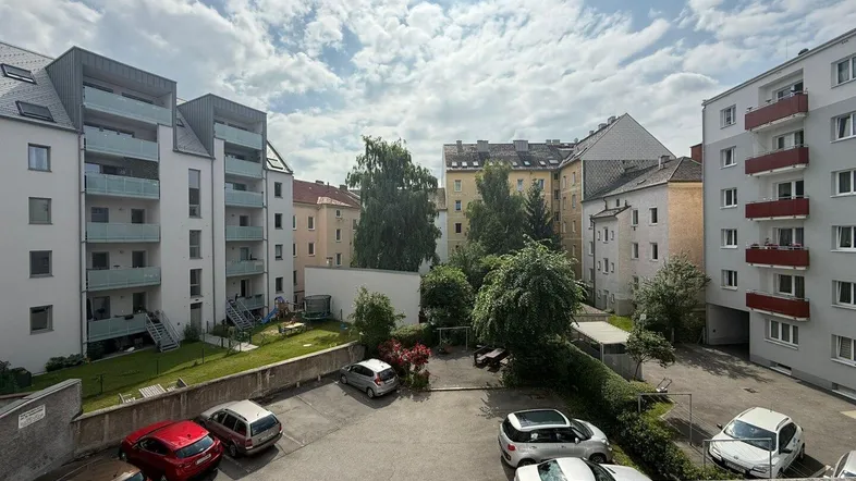 Blick auf den Innenhof mit Parkplätzen, Grünflächen und umliegenden Wohngebäuden unter bewölktem Himmel.